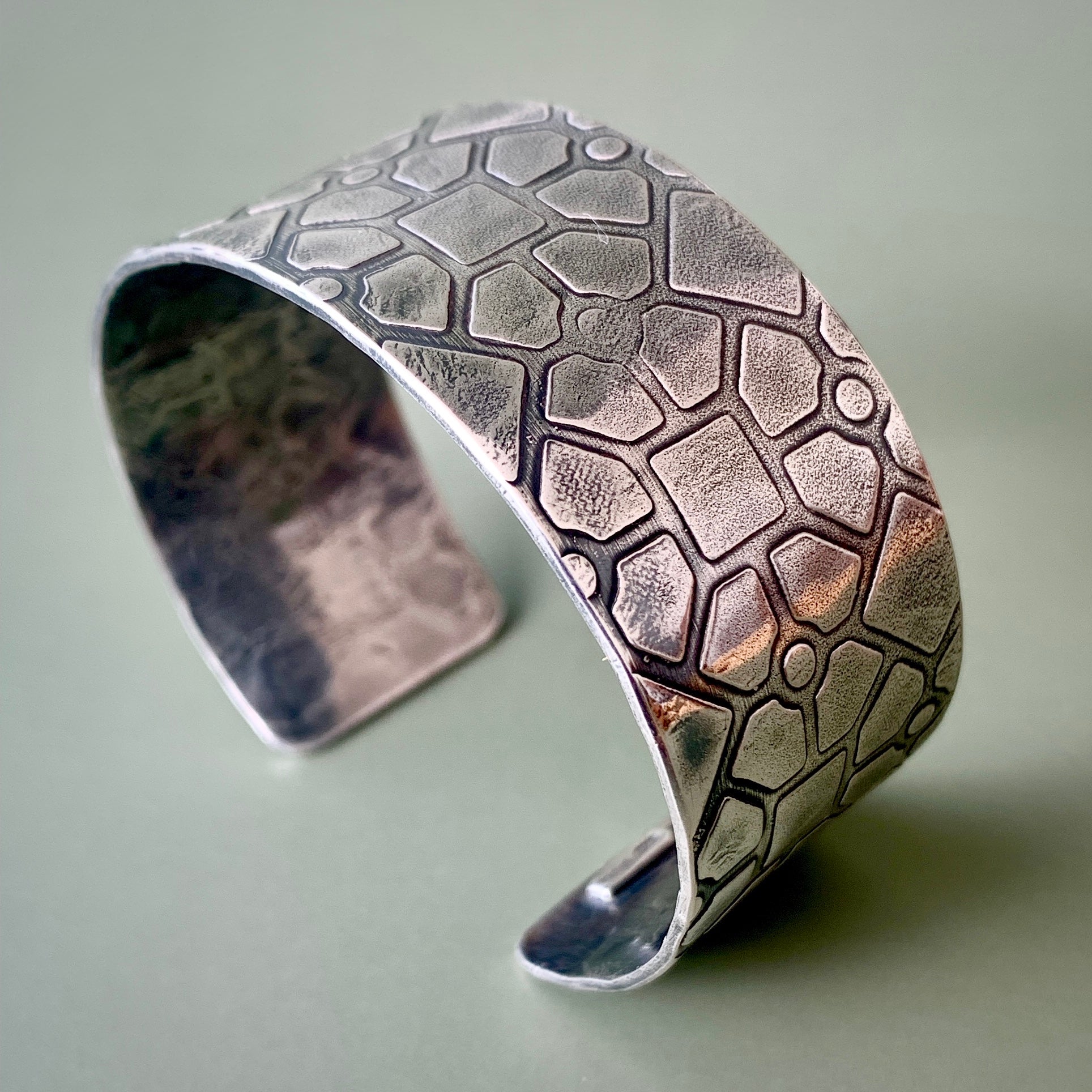 stelring silver hallmarked cuff with a geometric texture shown on a light green background