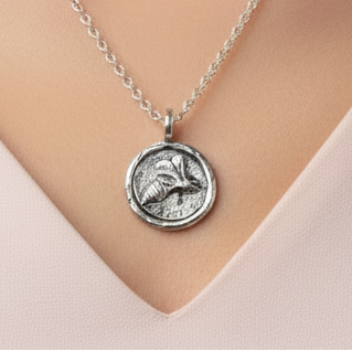 Woman in a v-neck top wearing a sterling silver round necklace with a border and an embossed bee within, Pendant has been oxiised to bring out the bee and hangs on a sterling silver belcher chain