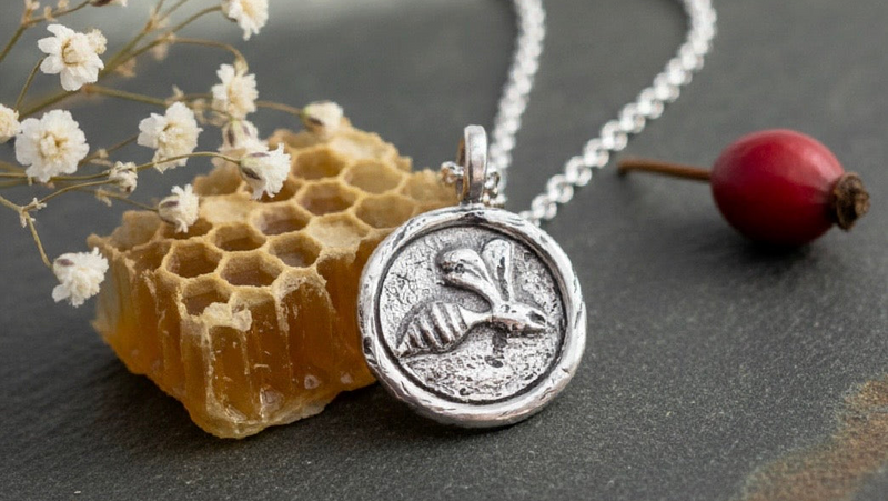 Sterling silver bee necklace with a belcher chain on a backdrop of honeycomb, white flowers and a red berry Nottingham