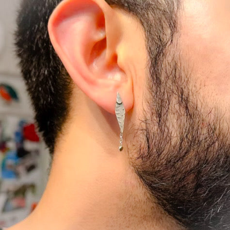 man with a beard wearing a diamond shaped earring with a tiny disc dangling from the diamond