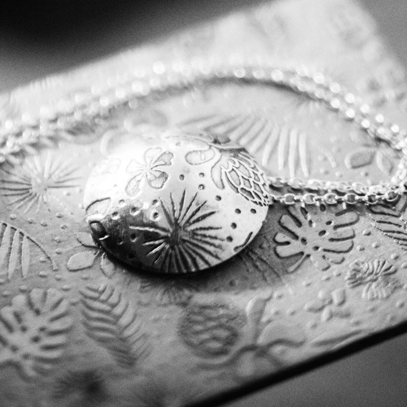 A silver patterned necklace laying on the texture plate that was used to create the pattern