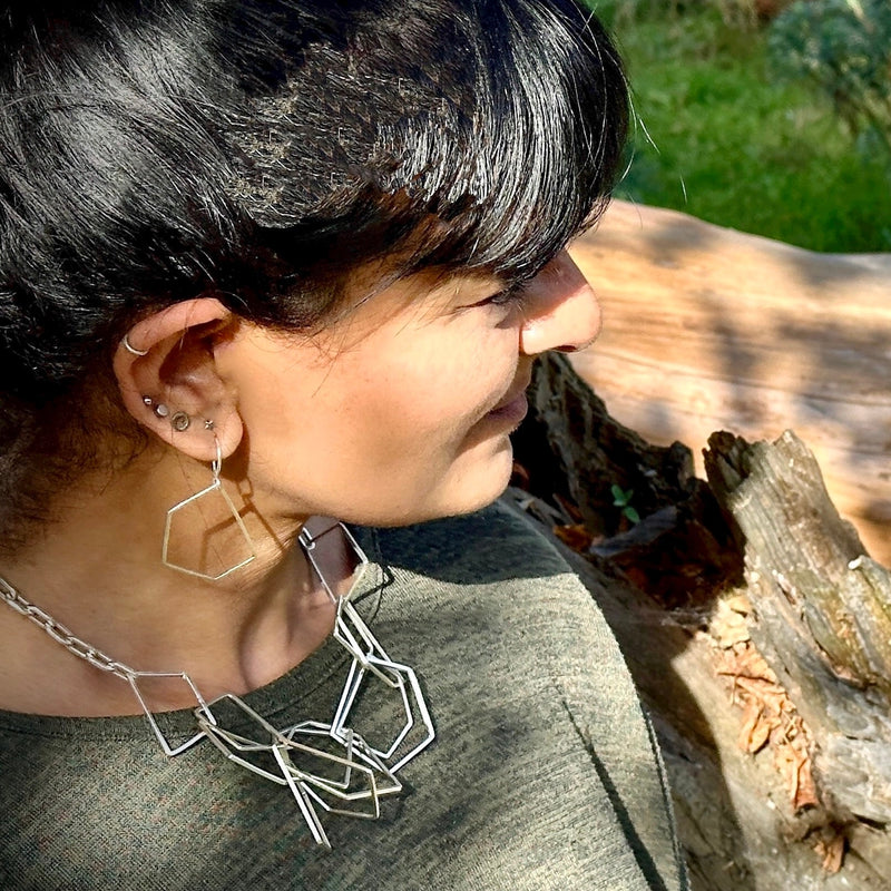 Indian woman with black hair wearing a handmade geometric silver necklace and silver earrings made in Nottingham