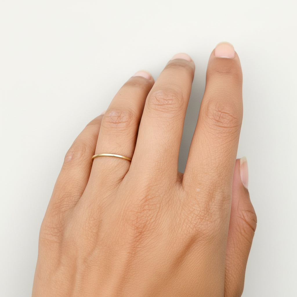 Hand wearing a skinny gold wedding ring band on a white background sustainable made by Bottlebee in Nottingham