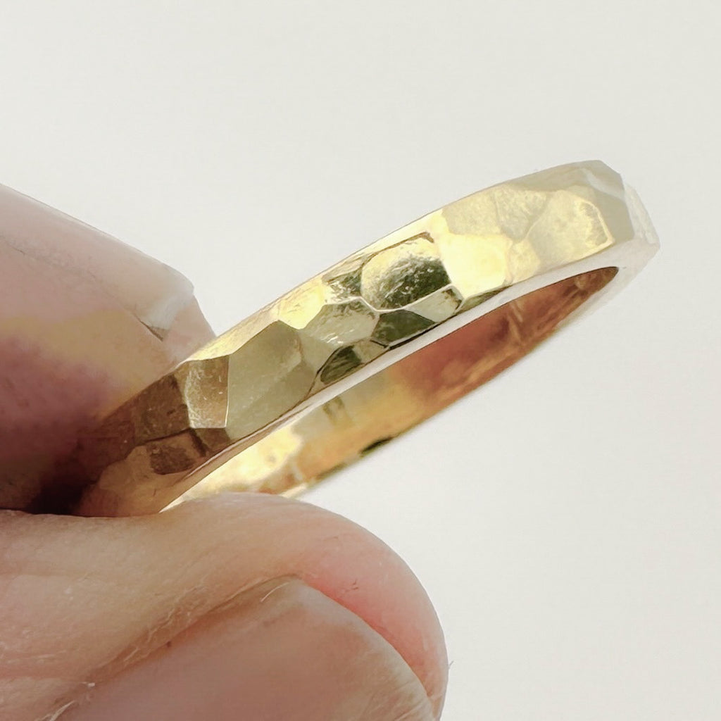 Gold ring with a hammered textured band held between fingers against a light background. Ring is bespoke and handmade in Nottingham by Bottlebee