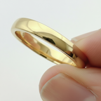 Gold ring with a textured band held between fingers against a light background 