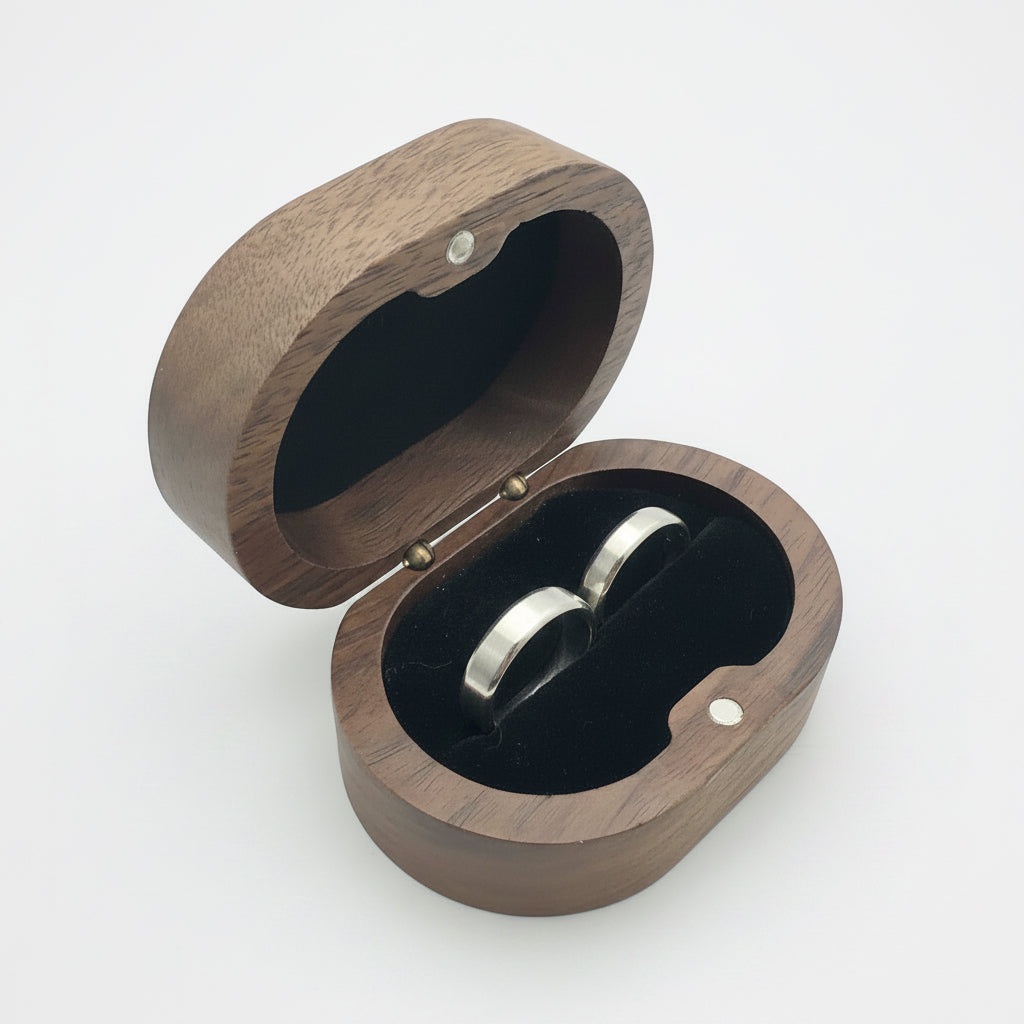 Wooden jewellery box with 2 couples silver wedding rings and bands inside on a light gray background