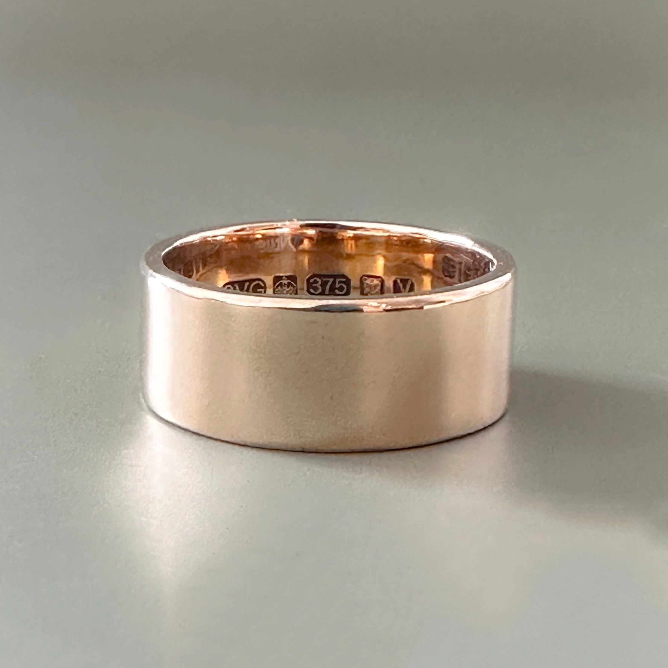 Solid gold wedding ring for men with visible hallmark on a light grey background