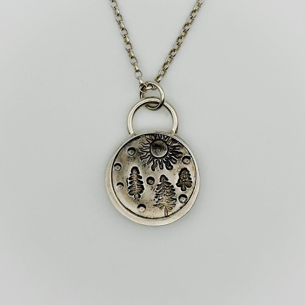Silver necklace with a round pendant featuring nature-themed designs on a light grey background