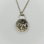 Silver necklace with a round pendant featuring nature-themed designs on a light grey background