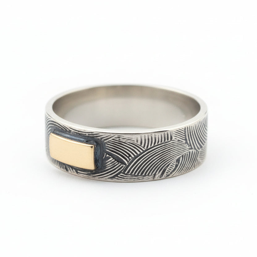 Silver and gold ring with textured design on a white background