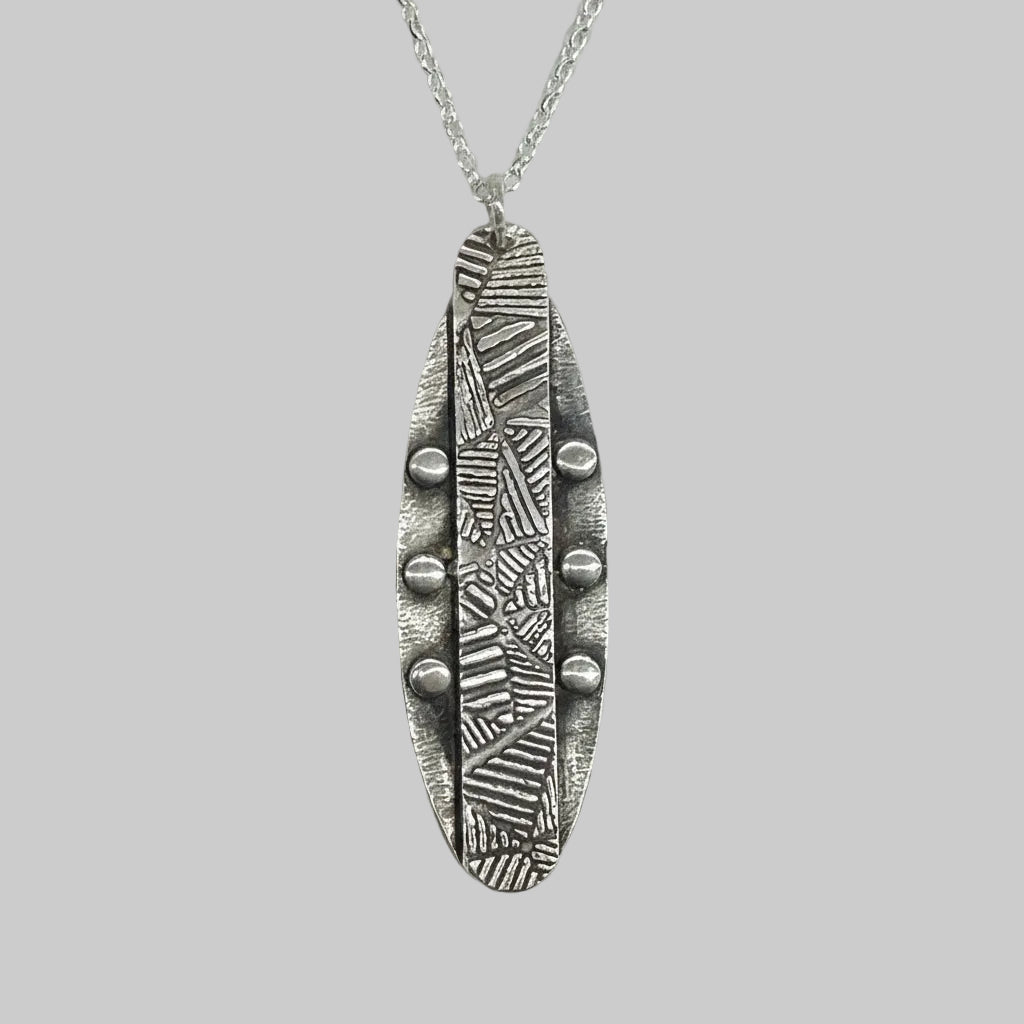 Bespoke handmade recycled sterling silver elongated oval shaped pendant with a geometric centre strip and small round elements wither side on a belcher chain against a light gray background