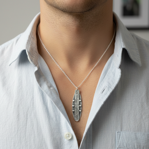 Man wearing an open neck light blue shirt wearing a handmade sterling silver textured and oxidised necklace made in Nottingham by Bottlebee