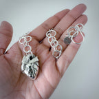 Hand holding a handmade necklace with a  heavy silver chain  and anatomical heart pendant. Jewellery is handmade in Nottingham by Bottlebee and is sustainable