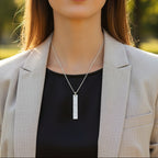 Woman wearing a grey jacked and a handmade bespoke silver bark textured bar pendant on a belcher chain against a grey background. Jewellery made by bottlebee