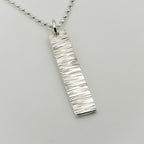 Sterling silver necklace with a bark textured pendant on a light grey background handmade jewellery by Bottlebee in Nottingham