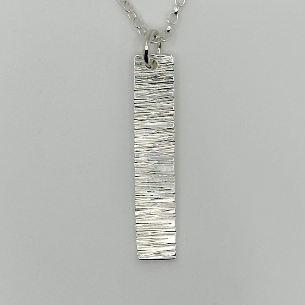 Close up of a sterling 925 silver bark textured pendant with a belcher chain necklace on a grey background