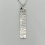 Close up of a sterling 925 silver bark textured pendant with a belcher chain necklace on a grey background