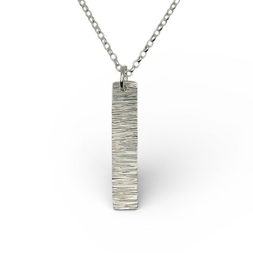 Silver necklace with a rectangular bark textured pendant on a white background