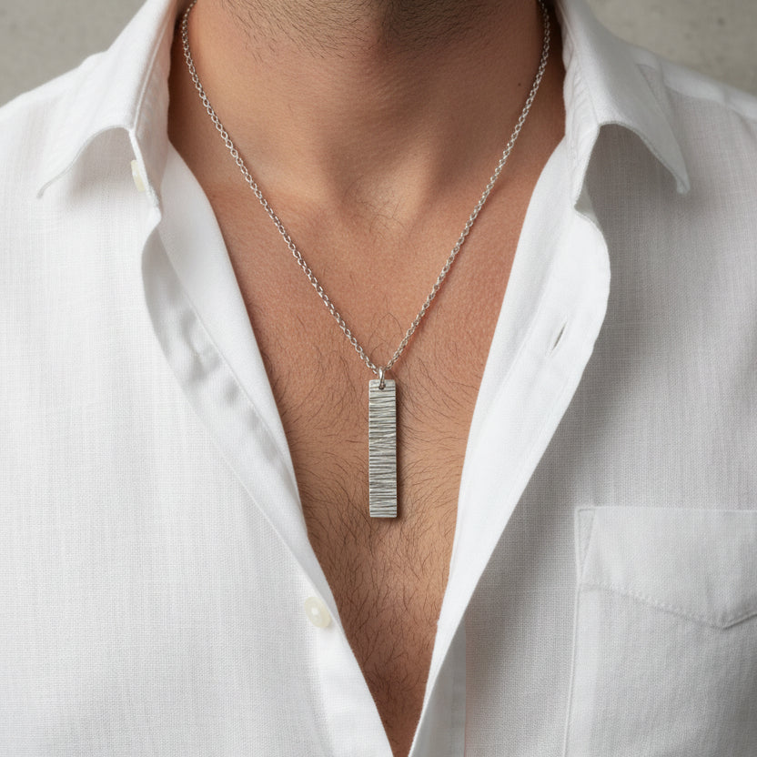 Man in a open necked white shirt wearing a silver unique bark textured pendant on a belcher chain handmade in Nottingham by Bottlebee