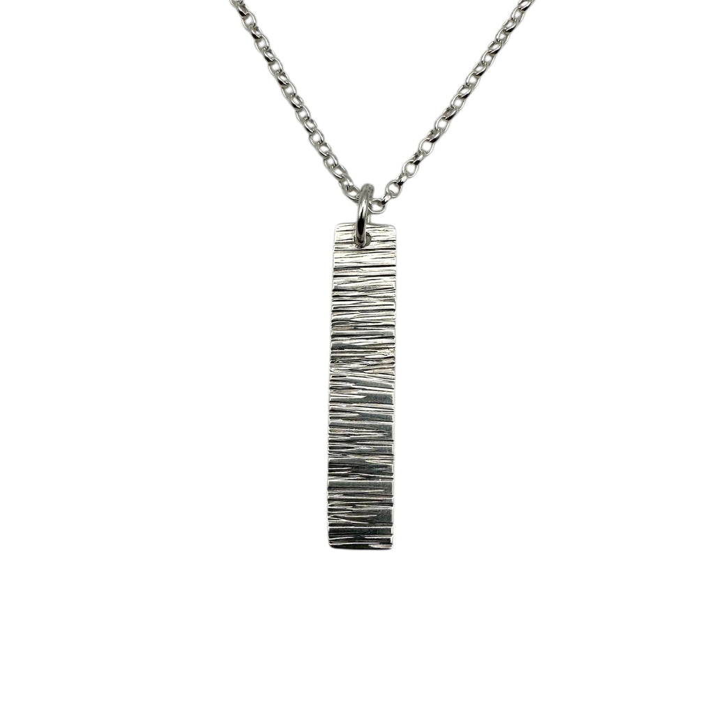 Silver necklace with a vertical bar pendant with a textured bark pattern on a white background