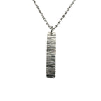 Silver necklace with a vertical bar pendant with a textured bark pattern on a white background
