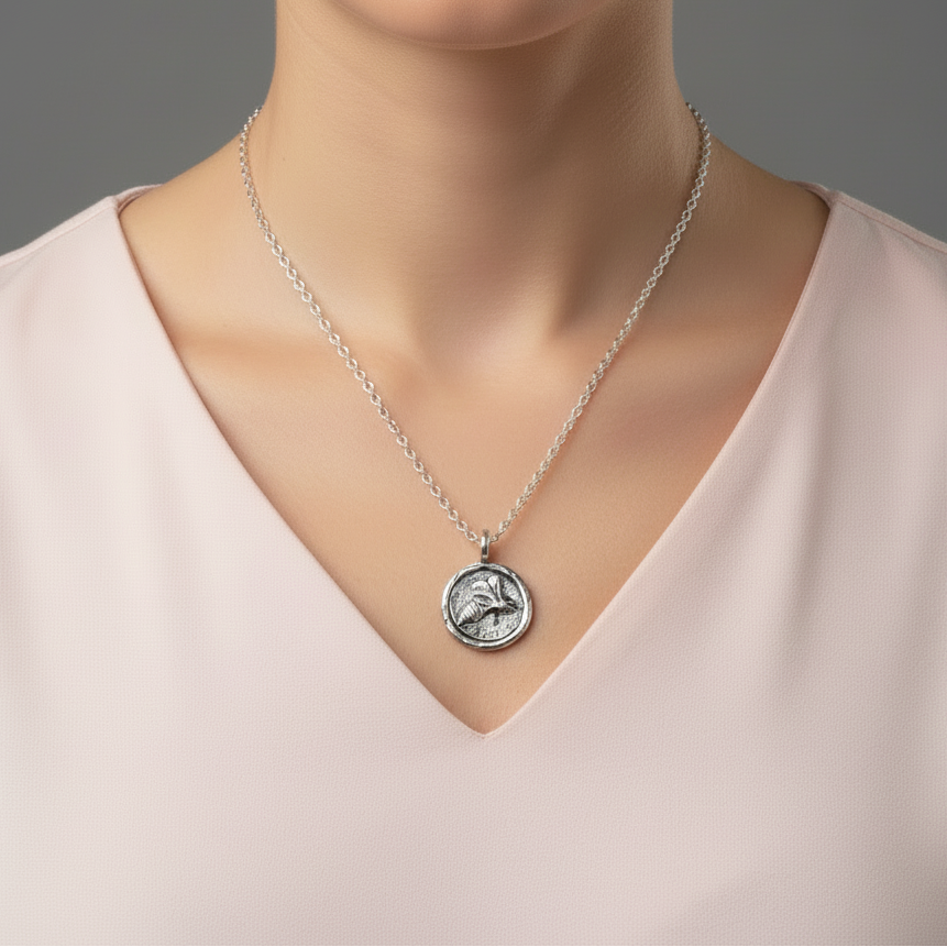 A woman with a gentle smile in a baby pink top wearing a handmade sterling silver bee necklace, jewellery made by Bottlebee in Nottingham