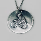 Close up of a handmade in Nottingham silver necklace with a pendant featuring a flea on a bicycle 
