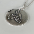 Close up of deaign of a silver handmade necklace with a round pendant featuring a unique flea on a bicycle wearing a top hat hamdmade by Bottlebee  who makes sustainable bespoke jewellery in Nottingham