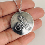 Silver necklace with a pendant featuring a design of a flea on a bicycle in a top had held on a hand, hamdmade by Bottlebee  who makes sustainable bespoke jewellery in Nottingham
