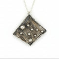 Handmade solid silver necklace with a textured square pendant on a light gray background