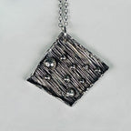 Handmade in Nottingham this sterling silver pendant with textured surface and embedded silver balls on a grey background sustainably handmade in Nottingham by Bottlebee