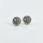Small sterling silver round stud earrings with intricate and oxidised dragonfly designs on a white surface handmade by Bottlebee who makes jewellery in Nottingham, commissions are welcome