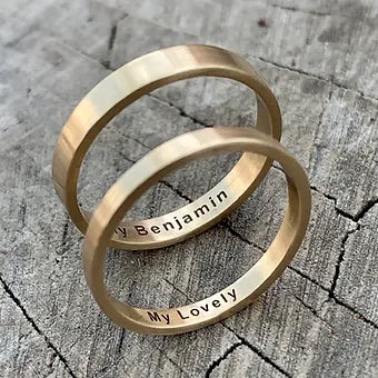 Two gold rings with engraved text on a wooden surface