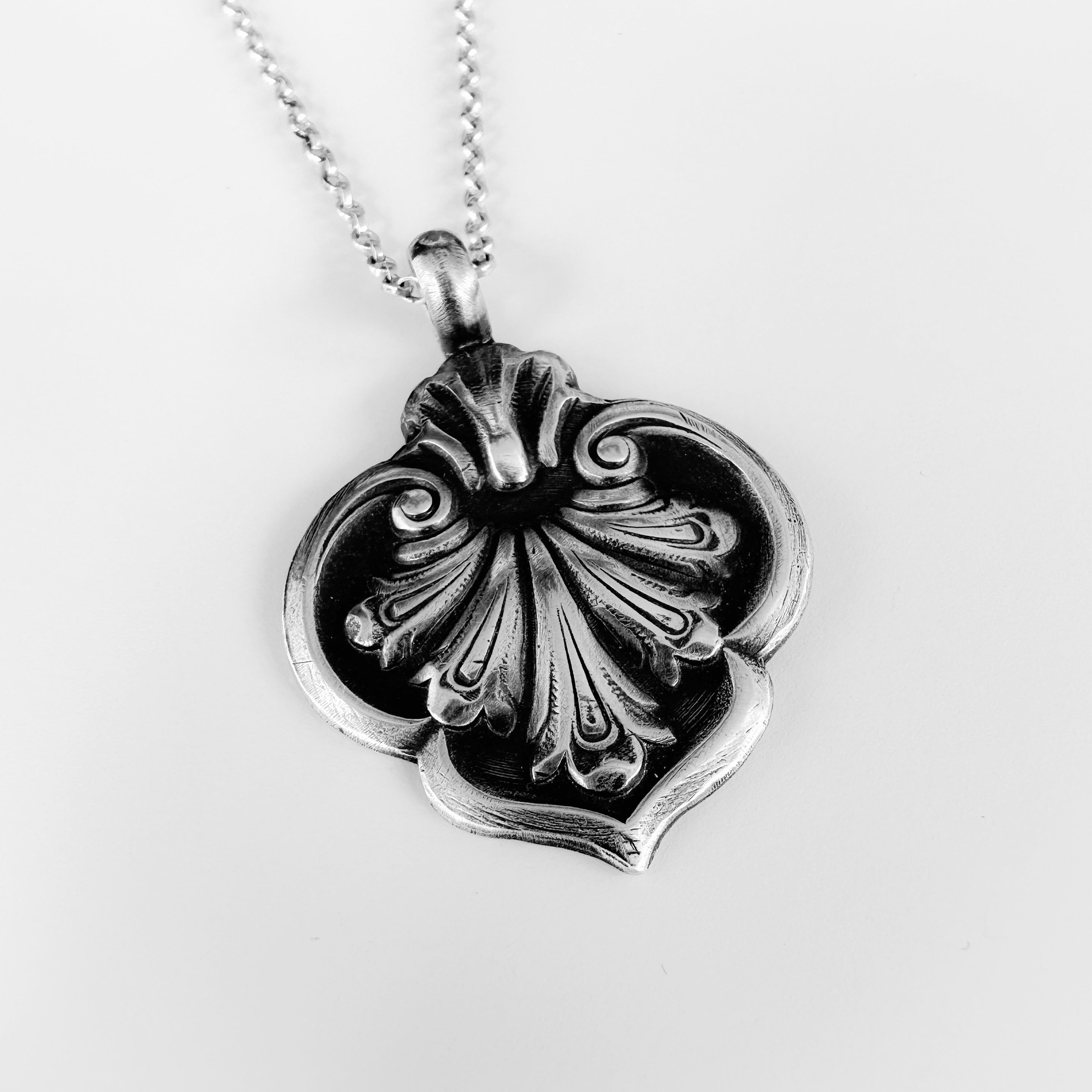 Silver flower pendant necklace which is oxidised on a white background