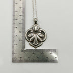 Silver necklace with an ornate pendant next to a ruler on a white background