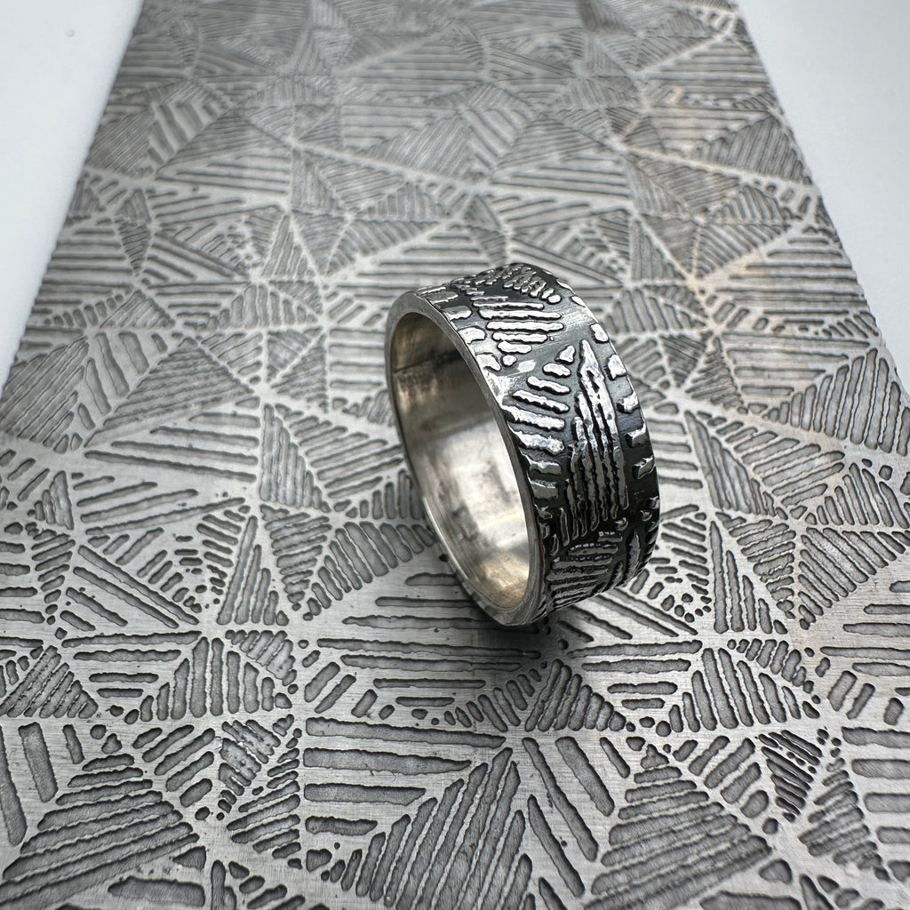 Solid sterling silver ring with textured geometric design on a textured metal geometric pattern surface handmade silverwedding ring nottingham