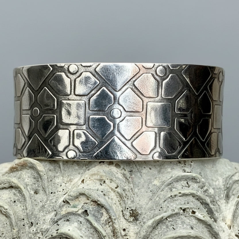 Silver cuff bracelet with geometric pattern on a textured surface