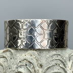 Silver cuff bracelet with geometric pattern on a textured surface