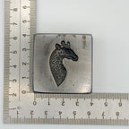 Metal giraffe stamp with giraffe design next to a ruler on a white background the silver will be pressed into the impression die to make the pendant