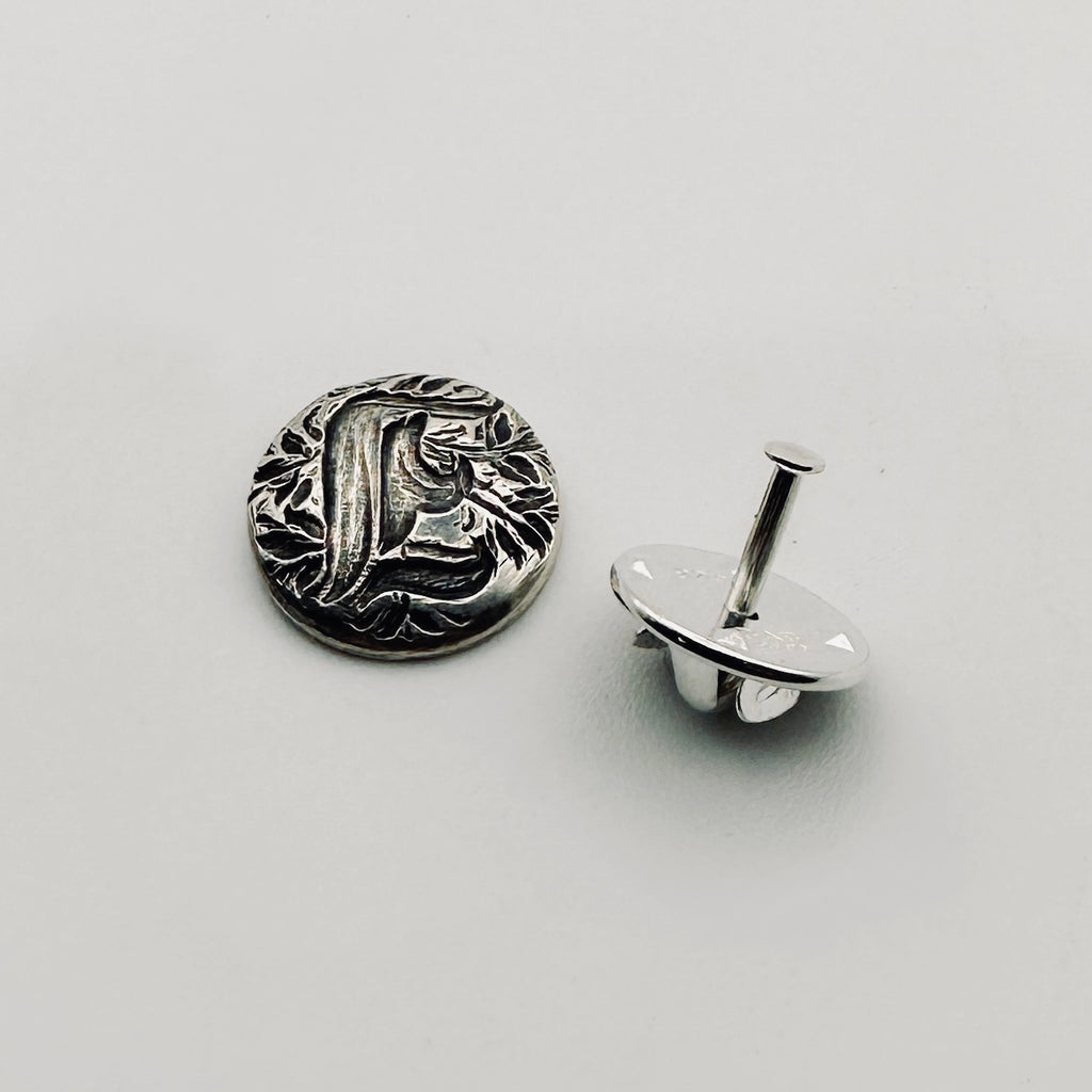 Silver decorative lapel pin with intricate personalised design on a light gray background