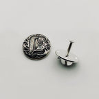 Silver decorative lapel pin with intricate personalised design on a light gray background