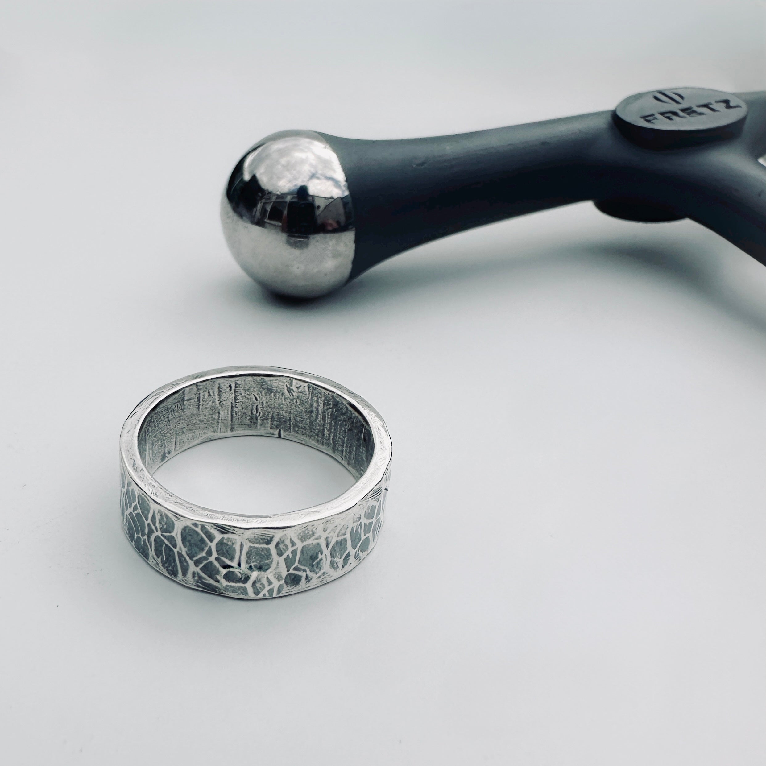 unique hammer textured sterling silver wedding ring band for a woman or man or unisex with textured surface next to a metal hammer on a light grey background handmade sustainable bespoke jewellery Nottingham