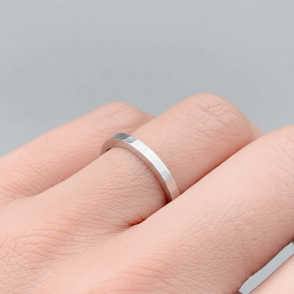 Solid sterling silver skinny wedding ring on a woman's finger on a light grey background handmade sustainable bespoke jewellery nottingham