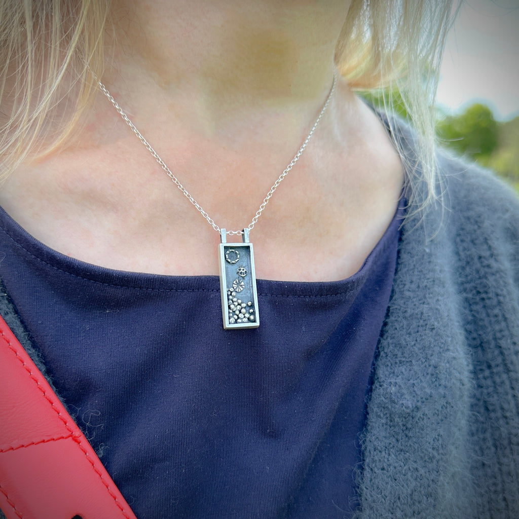 Person wearing a silver jewellery box necklace with a rectangular pendant with oxidised granules and accents handmade by Bottlebee in Nottingham