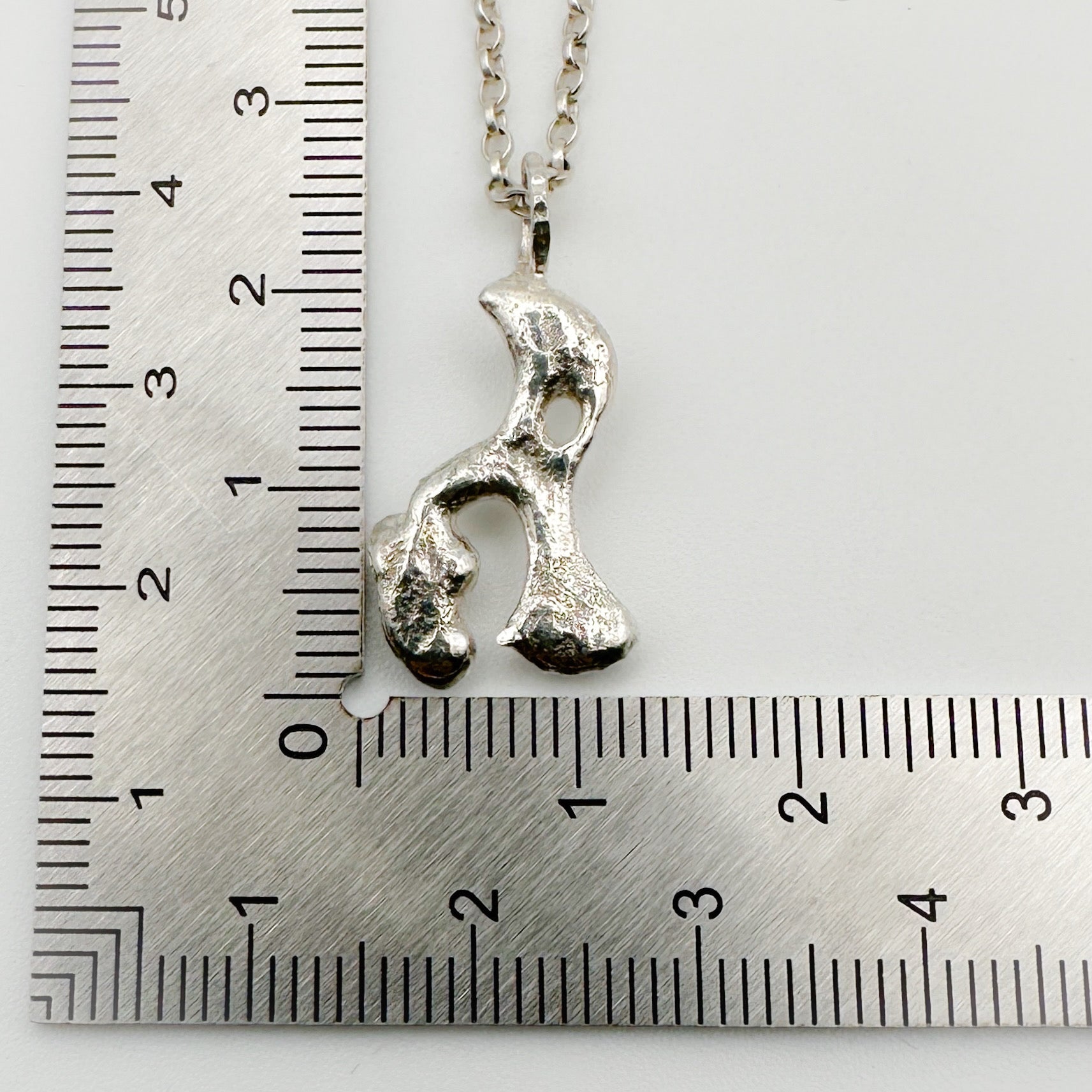 Silver pendant on a chain which has been sustainable made with recycled sterling silver next to a ruler for scale. Handmade bespoke jewellery in Nottingham