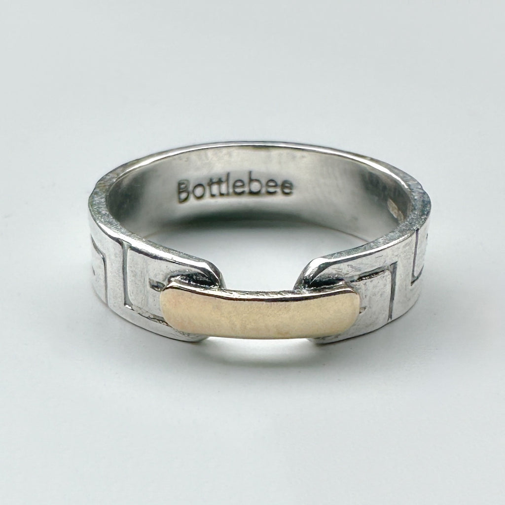 a silver and gold ring with Bottlebee stamped inside. The ring has a greek style pattern