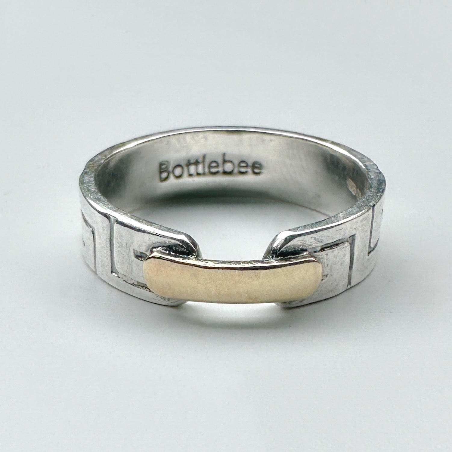 a silver and gold ring with Bottlebee stamped inside. The ring has a greek style pattern