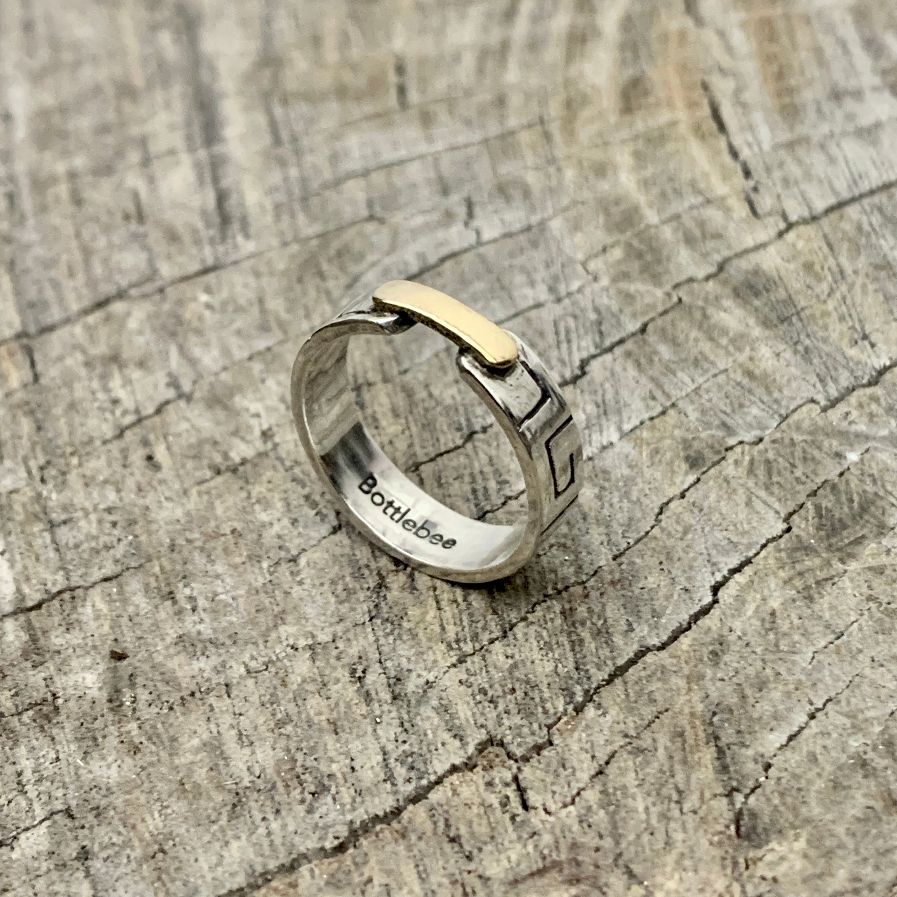 a silver and gold ring with Bottlebee stamped inside. The ring has a greek style pattern