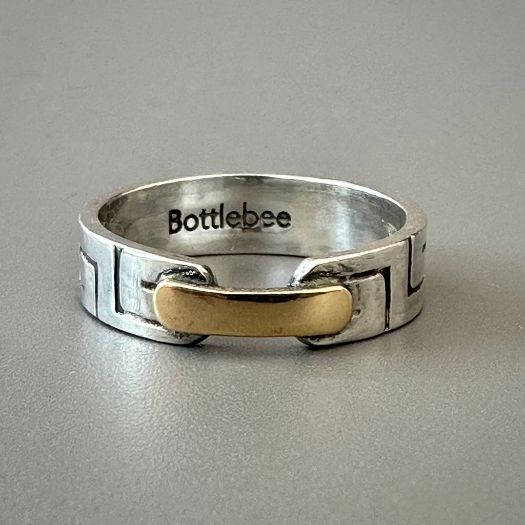 a sterling silver ring with a greek pattern and a gold bar joining t together