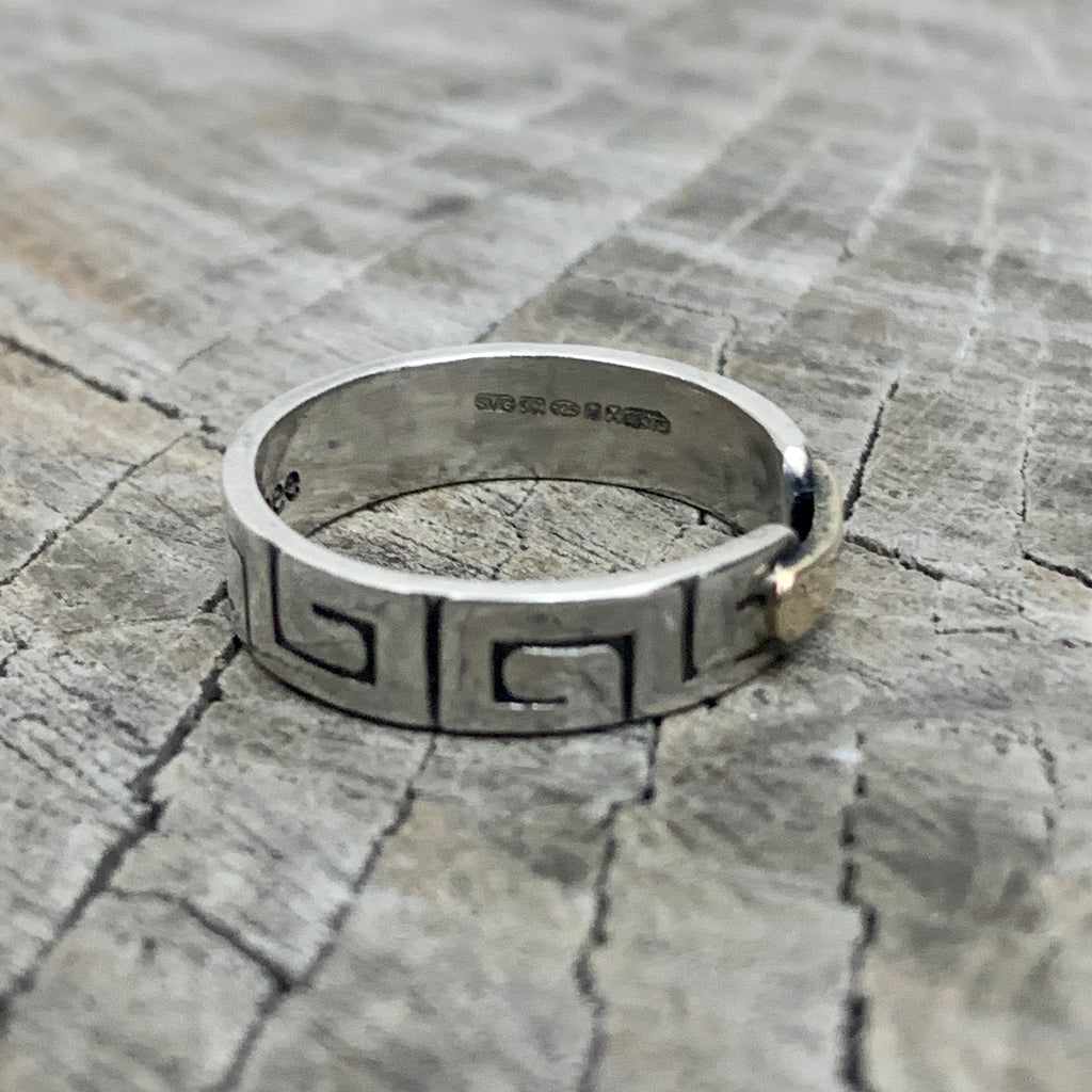 a hallmarked solid silver greek style ring with a gold bar on a wooden background